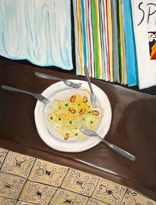 Plate of pasta with a fork and knife on a table with a colorful book in the background.