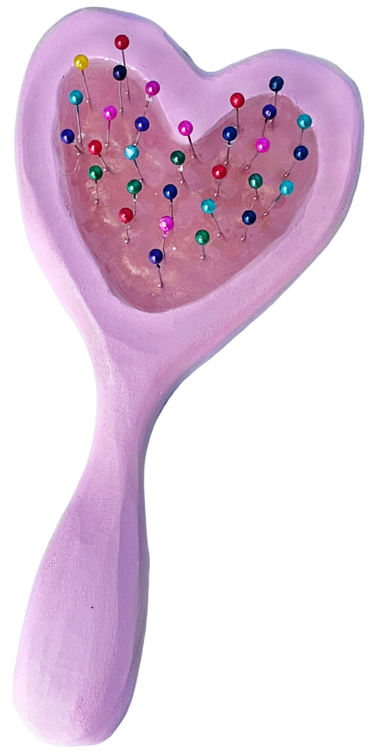 Pink heart-shaped hairbrush with colorful pins on a light gray background